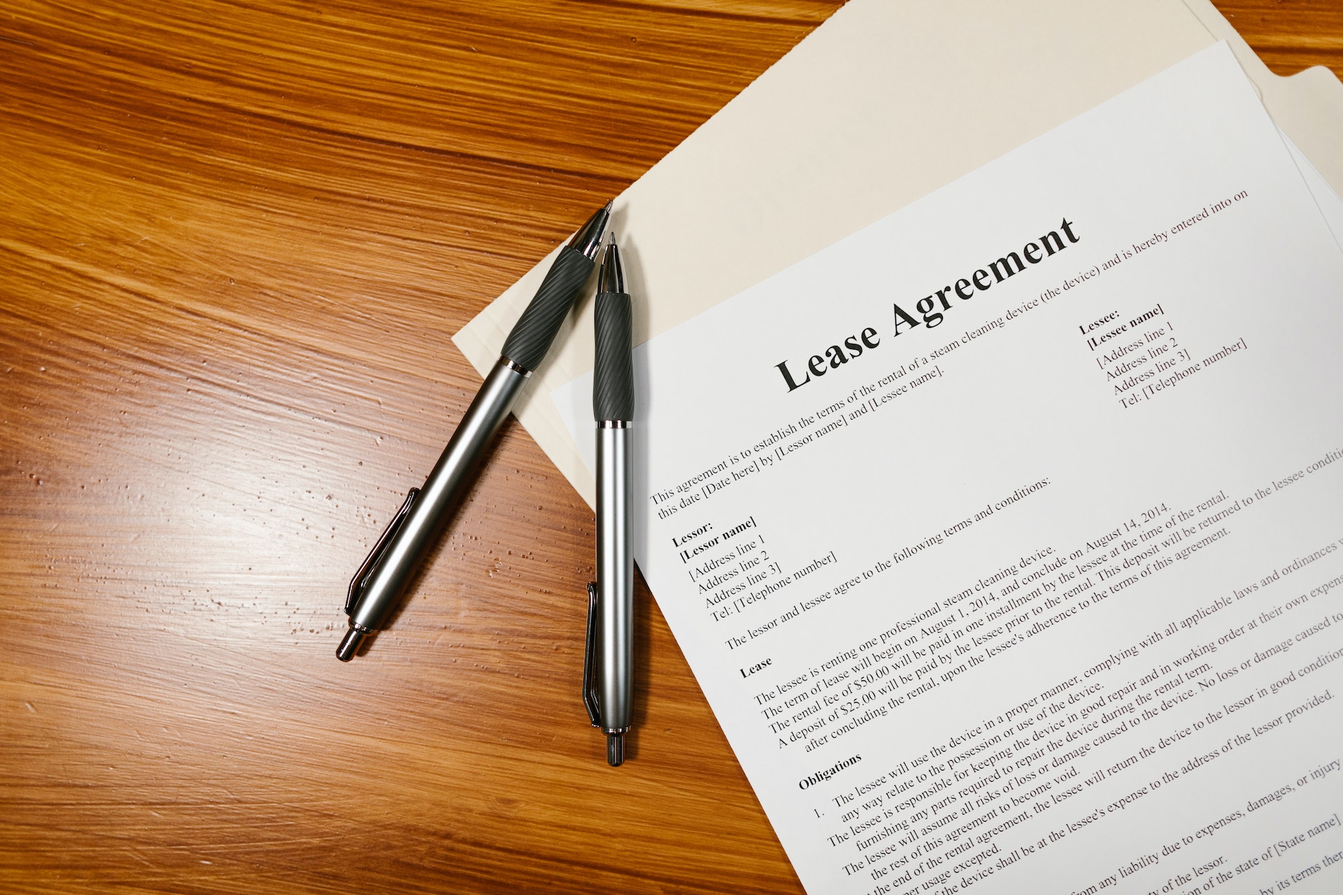 A photo of a lease agreement document on a wooden desk. Two black pens rest on top of the document.