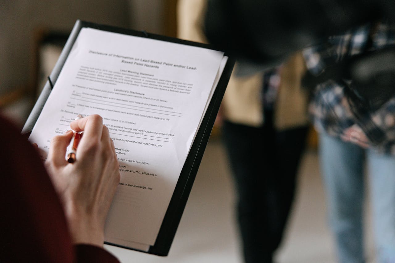 A photo of a lease agreement. A hand holding a pen skims the document. In the blurred background are two people.