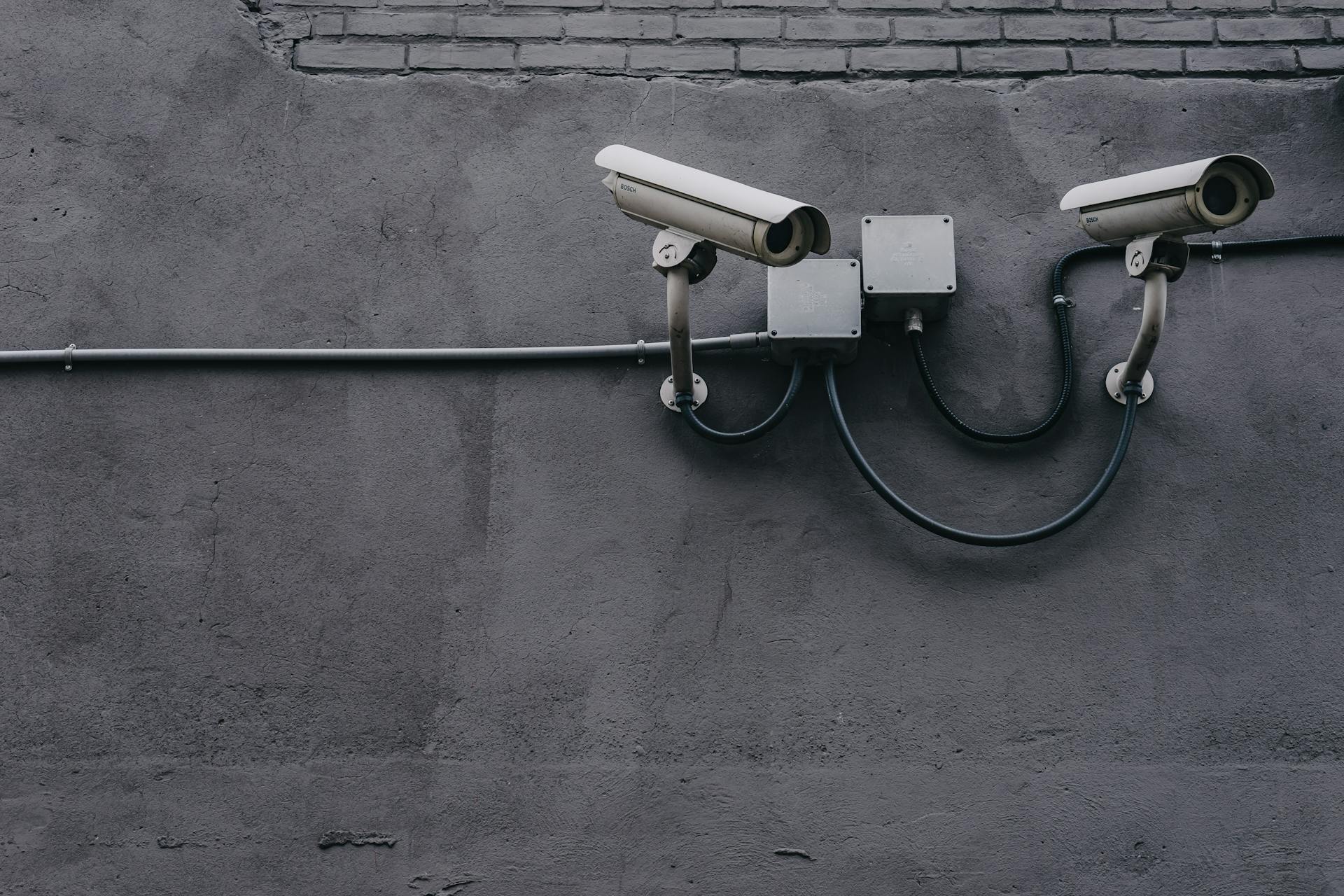 A photo of two security cameras mounted on a dark gray cement wall.
