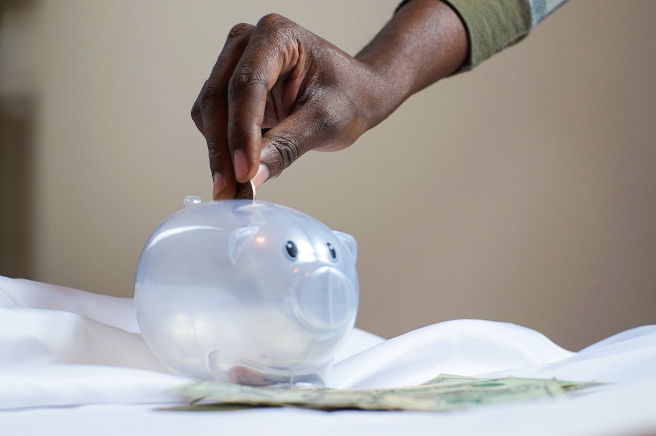 A picture of a hand placing coins into a transparent piggy bank