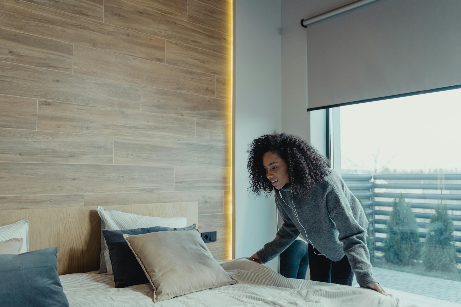 A woman in comfy clothes adjusts the bedding on a bed.