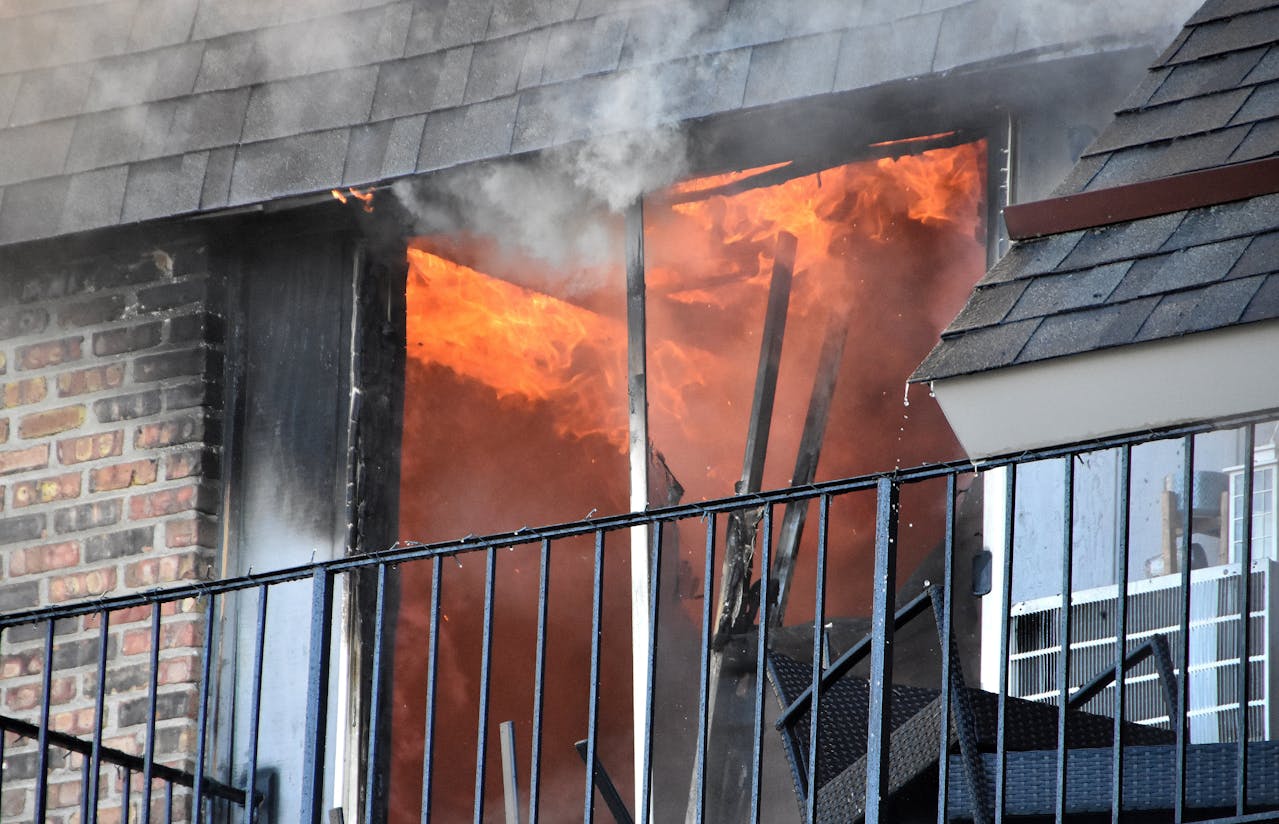 A room photographed from the outside of the building. The room is on fire, and smoke is billowing out of the shattered balcony doors.